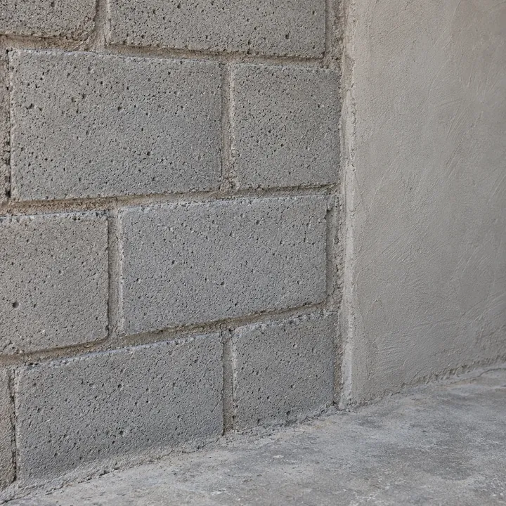 Parede de blocos de concreto poroso com juntas de argamassa e trecho rebocado.